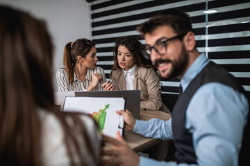 Group of four business people working together in their office on important project. They are talking and analyzing their business plan together.