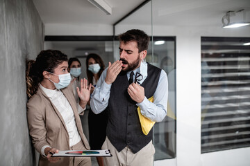 Group of business people with protective face masks against virus infection. One man is sick and he is coughing. Others are scared and trying to protect themselves.