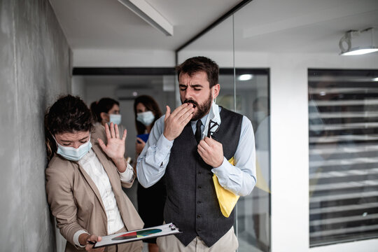 Group of business people with protective face masks against virus infection. One man is sick and he is coughing. Others are scared and trying to protect themselves. - Powered by Adobe