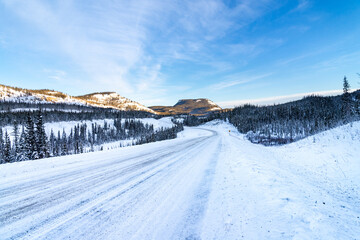 Long snow covered road in Yukon territories with snow coved mountains in back ground and frozen lake to the sid