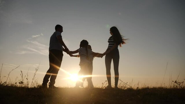 happy family mom dad and daughter play round dance silhouette at sunset. people in park kid dream concept. happy family parents with little kid child daughter play fun in park on grass holding hands