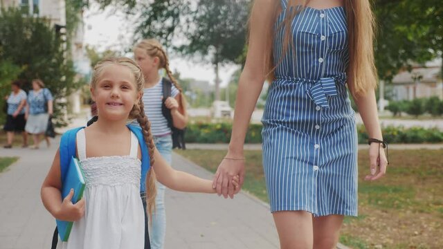 mom and daughter go to school. happy family school education concept. schoolgirl with mom go hand in hand to school on footpath in the park. little girl lifestyle with a briefcase time to study