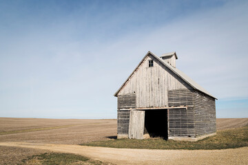 An Old Corn Crib by a Rural Gravel Road stands before an Open Farm Field © RR Photos