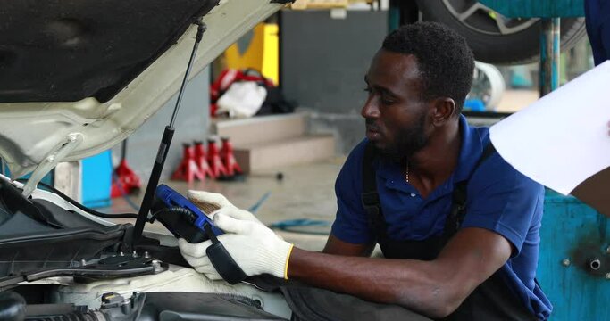 Professional car mechanic repair service and checking car engine by Diagnostics Software computer. Expertise mechanic working in automobile repair garage.