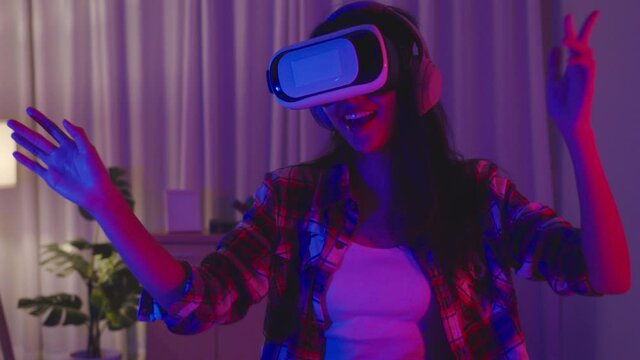 Young Asia lady wear VR headset having fun and dancing happy moment New Year neon night party event celebration in living room at home. Social distancing, quarantine for coronavirus prevention.