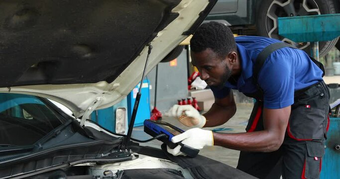 Professional car mechanic repair service and checking car engine by Diagnostics Software computer. Expertise mechanic working in automobile repair garage.