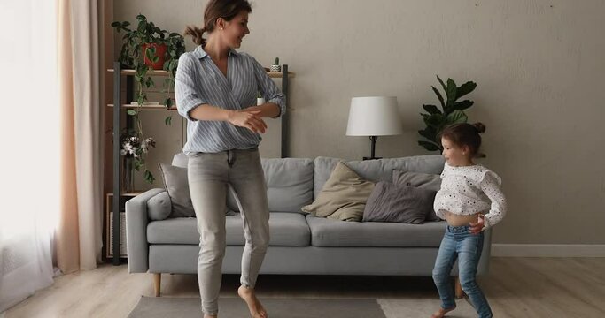 Active young mother little cute daughter dancing barefoot on carpet in modern cozy living room. Babysitter with small kid girl listen music spend time at home having fun. Teach child and hobby concept
