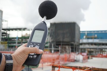 Hand of Environmental officer holding to use sound level meter for monitor is part of the prevention of environmental impacts at Chemical plant area or refinery factory.