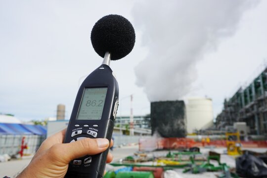 Hand of Environmental officer holding to use sound level meter for monitor is part of the prevention of environmental impacts at Chemical plant area or refinery factory.