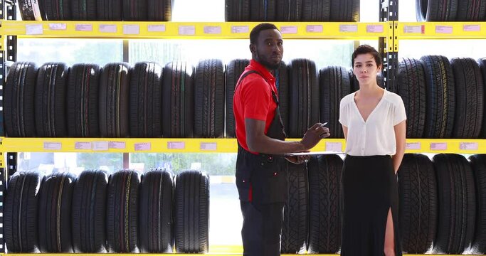 Salesperson and menager explaining the quality of the product to the woman customer. maintenance and auto service garage concept. Saleman showing wheel tires