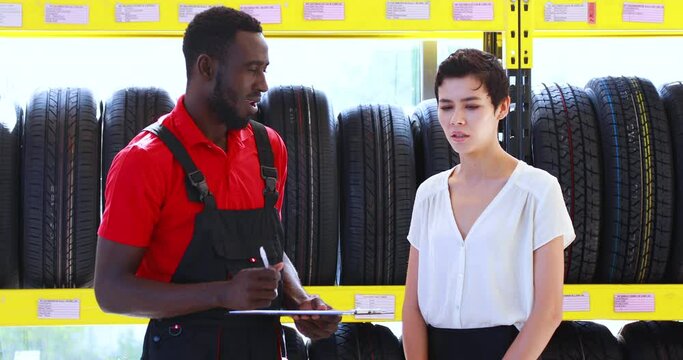 Salesperson and menager explaining the quality of the product to the woman customer. maintenance and auto service garage concept. Saleman showing wheel tires