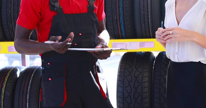 Salesperson and menager explaining the quality of the product to the woman customer. maintenance and auto service garage concept. Saleman showing wheel tires