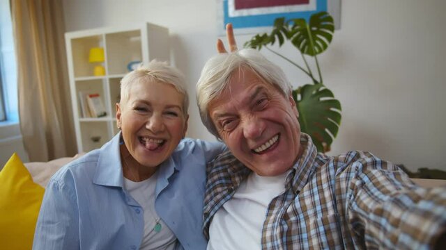 Happy active senior caucasian couple sitting on sofa and taking selfie