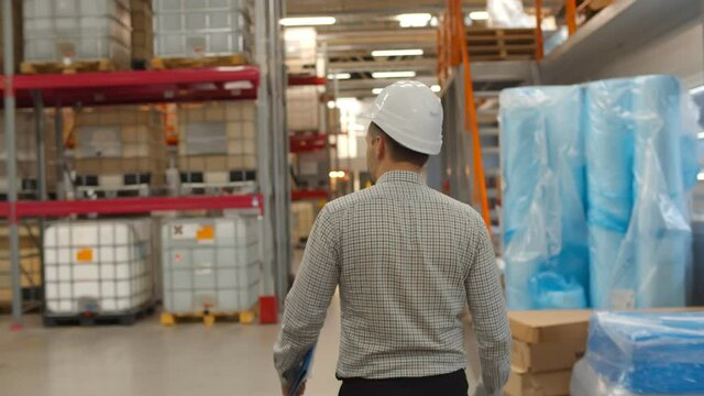 Back view of manager and supervisor in hardhat discussing inventory in factory warehouse.