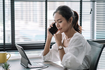 Attractive and successful asian businesswoman working in modern office, talking on phone with client at their desk.