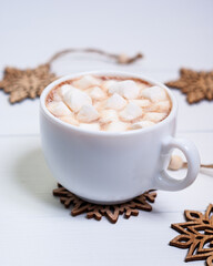 Cup of coffee or hot chocolate with marshmallows and wooden snowflakes on white wooden table. Creative winter arrangement.