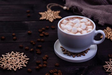 Obraz na płótnie Canvas Cup of coffee with marshmallows and wooden snowflakes on dark wooden table. Winter concept, dark mood photo.