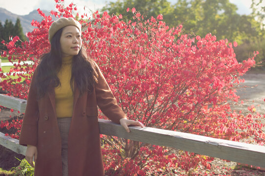 Young Asian Woman Wearing Fall / Autumn Attire Leaning By A Fence