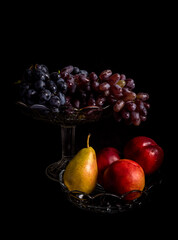 Fototapeta na wymiar Crystal vases with grapes, peaches and pear on a black background