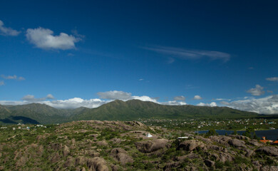 Panorama view of El Cajon lake, in Capilla del Monte, Cordoba, Argentina. The pure water lagoon, rocky mountains, green forest and rural town buildings under a deep blue sky in a summer day.