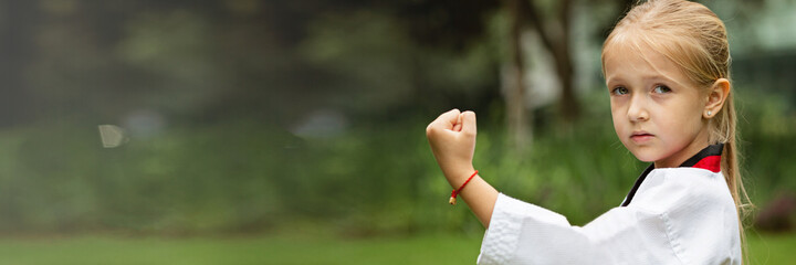 Caucasian little girl six years old in kimono with white belt exercising Taekwondo at summer park...