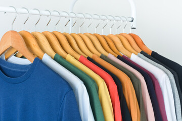 close up collection of colorful t-shirts hanging on wooden clothes hanger in closet or clothing...