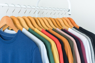 close up collection of colorful t-shirts hanging on wooden clothes hanger in closet or clothing...