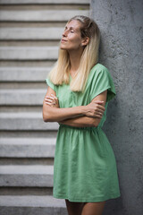 Blond woman in standing next to the grey wall in green linen cotton dress 