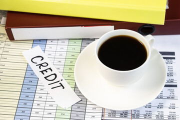 on business documents there is a white Cup of coffee near the folder and a white sheet on which credit is written.