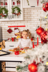 Little girl prepares Christmas cookies in the kitchen decorated for the holiday