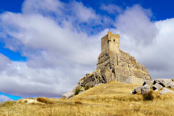 Castillo medieval de Atienza Guadalajara, alzándose en la colina con cielo azul y camino de tierra hacia el castillo.
