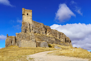 Fototapeta na wymiar Castillo medieval de Atienza Guadalajara, alzándose en la colina con cielo azul y camino de tierra hacia el castillo. 