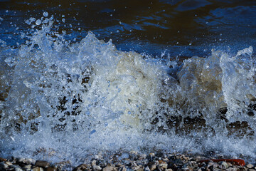 waves run onto the shore and crash against the rocks, creating many splashes and splashes near the shore. river surf in stormy weather near a stone pebble coast with foamy splashing waves.