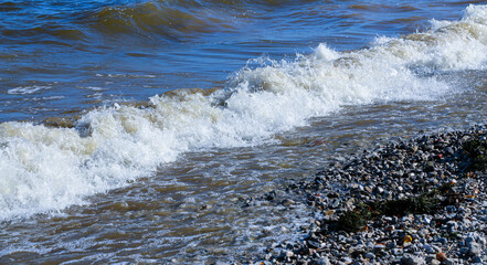 waves run onto the shore and crash against the rocks, creating many splashes and splashes near the shore. river surf in stormy weather near a stone pebble coast with foamy splashing waves.