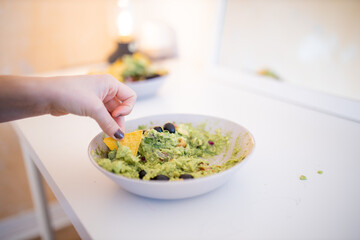 Female hand dipping nachos in guacamole sauce with olives
