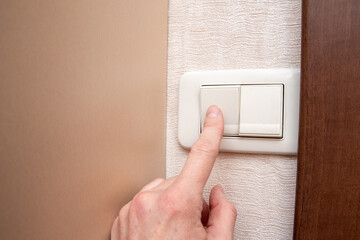 Close-up of a woman's hand turning the light on or off with a wall switch, front view, close-up, copy space