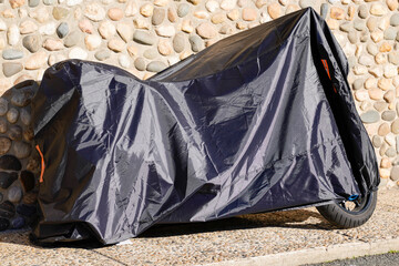 motorbike protected by outdoor protective cover in street motorcycle with dark grey bike tarpaulin jacket