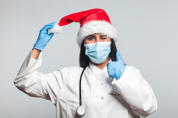 Fototapeta na wymiar Portrait of a medical doctor wearing a santa claus hat with a protective mask on his face against covid-19 coronavirus infections and turns thumbs up, concept of Christmas work in hospital