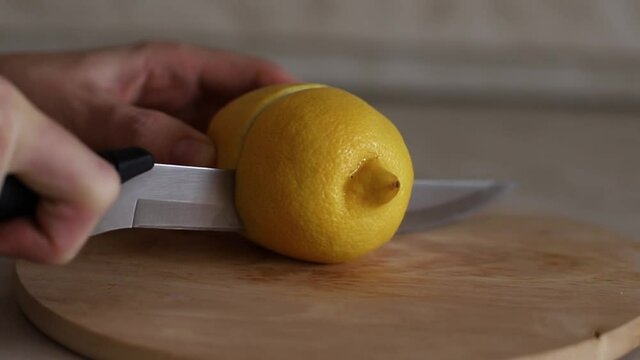Close-up view of a lemon cut in half with a knife on a wooden cutting board. Slicing lemon. Sour fruit. Cold treatment.