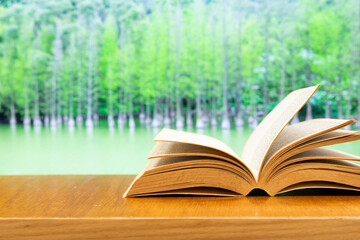 old book open on a wood table with blurred beautiful cypresses in a calm lake as background