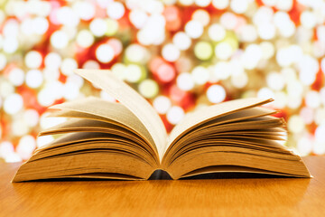 open old book on a wood table with blurred colourful sparking lights as background.