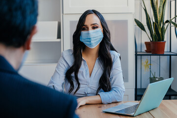 Portrait of a business woman at meeting sitting at desk with customer wearing face mask for social distancing due to coronavirus - Powered by Adobe