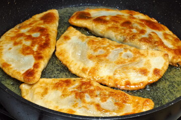 Almost ready pasties are fried in hot oil in a pan.