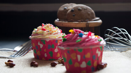Cupcakes with cute colourful tiny topping in different shapes and Chocolate chips cookies on the black background, text and copy space available.