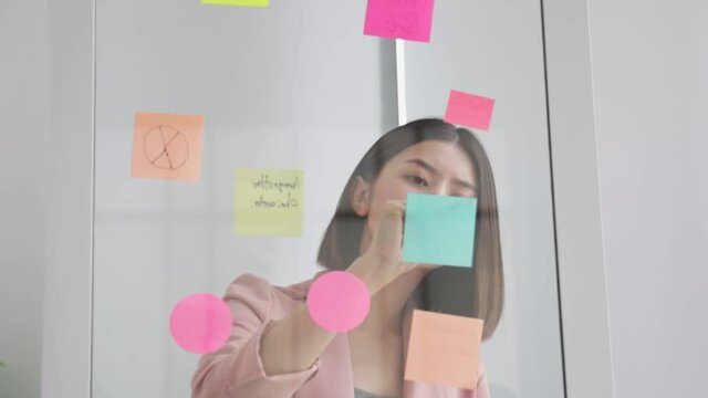 Asian freelance  business woman  working while working  at  office . girl working overtime, enjoy relax time.female working  writing one post it white board.