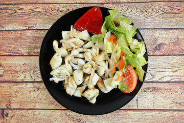 Portion of grilled cuttlefish garnished with lettuce and red pepper, on wooden table