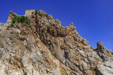The peak of the rock with the wall of the Alanya Castle at the top (Turkey). Rough stone clump against the blue sky, close-up