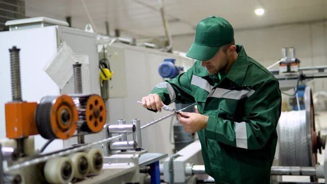 factory worker in a robe and cap checks the performance of the device for the production of cable products from a copper core