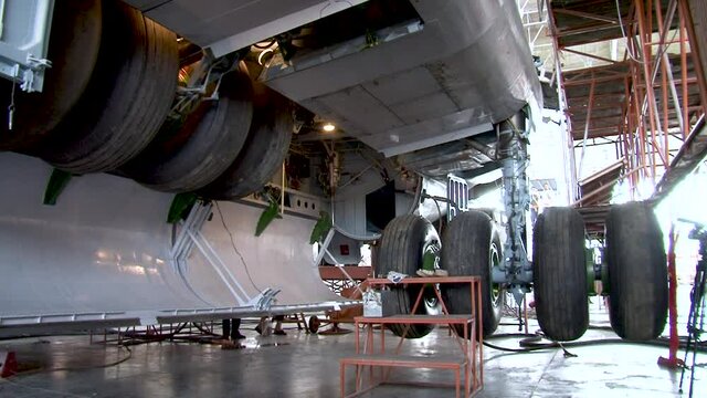 Maintenance of IL-76. Chassis niche doors to open. Rackes chassis move down. Niche chassis doors to closed. Close-up.  Plane stands on hydraulic elevators.