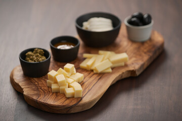Wood board with cheese, olives and sauces on walnut table
